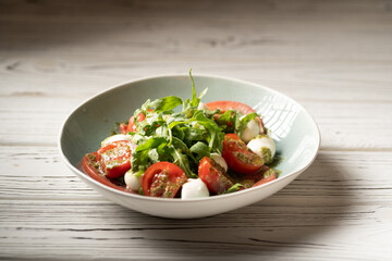 Italian caprese salad in restaurant. Fresh mozzarella, cherry tomatoes and basil leaf with pesto...