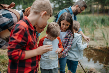 Young students analyzing water quality, ph level with indicator strips during biology field teaching class. Female teacher during outdoor active education.