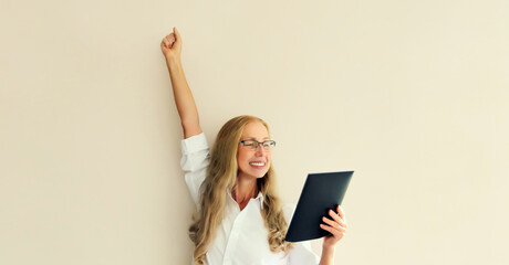 Happy joyful mature woman employee with tablet computer celebrates victory, feels success