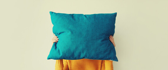 Healthy sleep, woman holding colorful soft pillow covering her head at home in morning