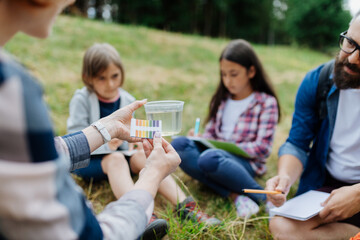 Young students analyzing water quality, ph level with indicator strips during biology field...