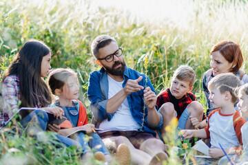 Fototapeta premium Young students learning about nature, forest ecosystem during biology field teaching class, observing wild plants. Dedicated teachers during outdoor active education.
