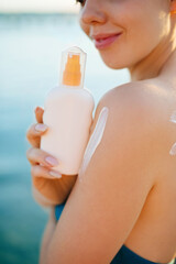 Close up of young woman putting sun cream on shoulder. Girl applying  sunscreen