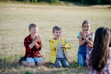 Children sitting on grass on meadow playing clapping game. Dedicated teachers during outdoor active education teaching about ecosystem, ecology.