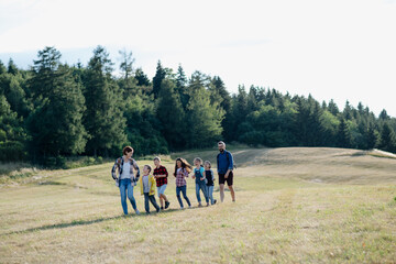 Young students walking across meadow during biology field teaching class, holding hands. Dedicated teachers during outdoor active education teaching about ecosystem, ecology.