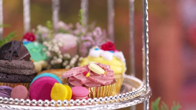 Afternoon Tea or High Tea Display in the silver rack with flowers, macaron, scone, cake, cup cakes, on colorful background