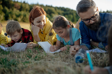 Young students learning about nature, forest ecosystem during biology field teaching class, writing...