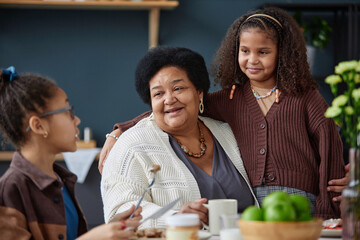 Portrait of happy African American grandmother with two girls enjoying time together in kitchen