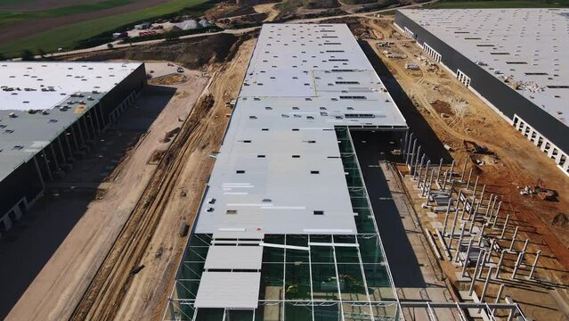 Aerial view of construction site with warehouse building under construction for storage. Assembling industrial building with steel frame structure and roof truss. Infrastructure for logistics