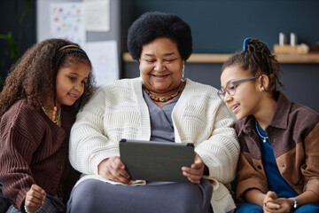 Front view portrait of smiling senior Black woman using digital tablet at home with two young girls...
