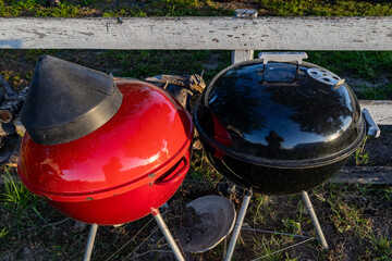 SOlomons, Maryland USA A red and a black grill stand besides each other in the morning light.
