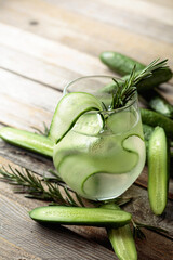 Gin tonic with ice, rosemary, and cucumber on an old wooden table.