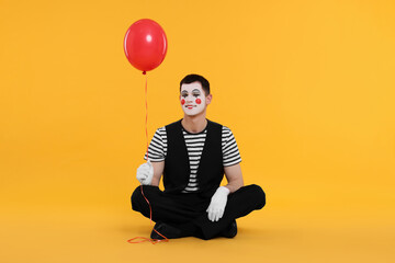 Funny mime artist with balloon on orange background