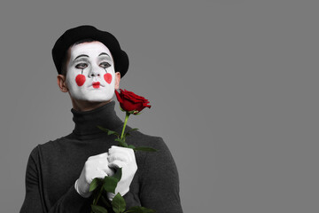 Portrait of mime artist with red rose on grey background. Space for text