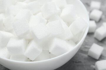White sugar cubes in bowl on grey table, closeup