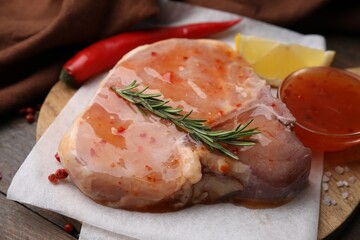 Board with raw marinated meat, rosemary and spices on wooden table, closeup