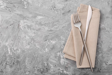 Elegant silver cutlery and kitchen towel on grey textured table, top view. Space for text