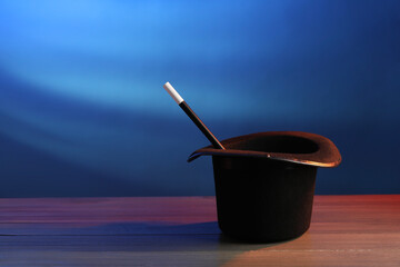 Magician's hat and wand on wooden table against blue background, space for text