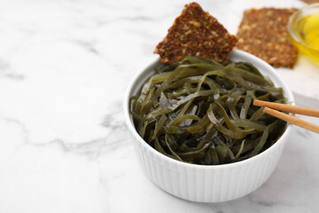 Tasty seaweed salad in bowl served on white marble table, closeup. Space for text
