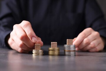 Taxes. Woman with wooden cubes and coins at grey table, closeup