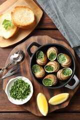 Delicious cooked snails in baking dish served on wooden table, flat lay
