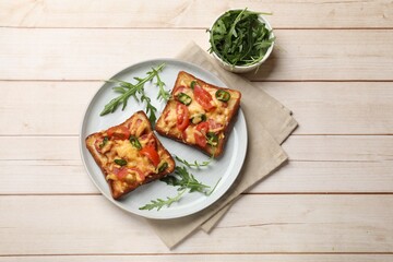 Tasty pizza toasts and fresh arugula on light wooden table, flat lay