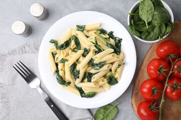 Tasty pasta with spinach and sauce served on grey textured table, flat lay