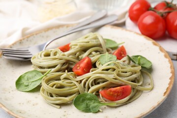 Tasty pasta with spinach, tomatoes and cutlery on light table, closeup