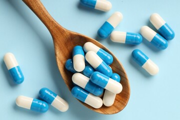 Antibiotic pills and spoon on light blue background, top view