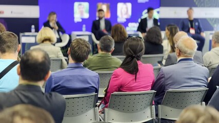 Audience members attentively listening to speakers at a business conference. Focus is on engagement and professional development in a corporate setting.