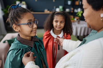 Close up of African American senior woman helping girl putting on costume cape at home