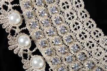 Fragment of a lace necklace with stones and pearls isolated on a black background, close-up.