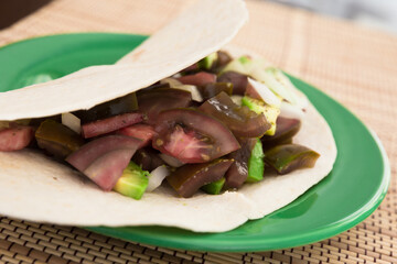Salad of black tomatoes, avocado and onions in Italian tortilla on green plate