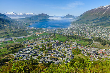 Dawn breaks over a picturesque town nestled among mountains with a fjord shrouded in mist.