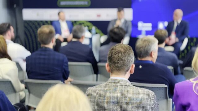Audience of business professionals attentively listening to speakers during a corporate conference panel with blurred background emphasizing focused attention and learning.