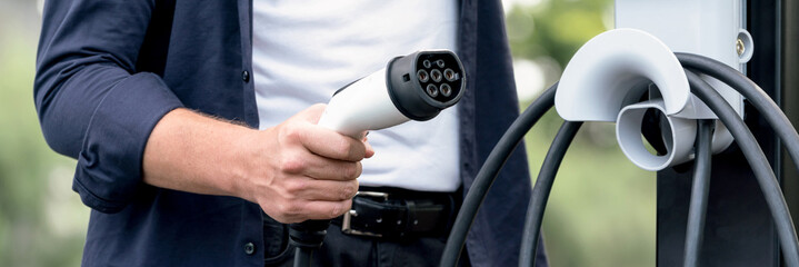 Man recharging battery for electric car during road trip travel EV car in natural forest or...