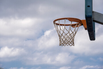 A Shot from the side of a basketball hoop with blue sky with clouds in the background and space for text.