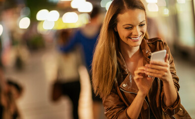 Young woman using smartphone downtown in the city at night