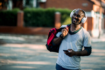 Happy man with gym bag and headphones using smartphone