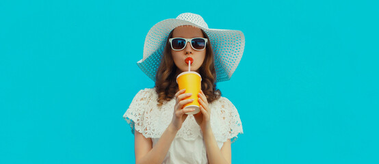Summer portrait of beautiful young woman with cup of fresh juice wearing hat on blue background