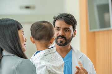 Confident Indian male doctor talking to mother and child patient in hospital