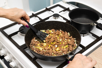 housewife frying minced meat with onions in a frying pan.