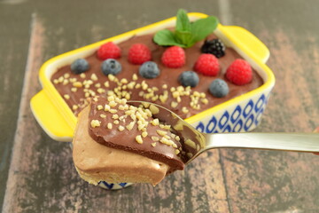 Homemade oatmeal tiramisu with melted dark chocolate topped with fresh berries, chopped almond and mint leaf on serving dish