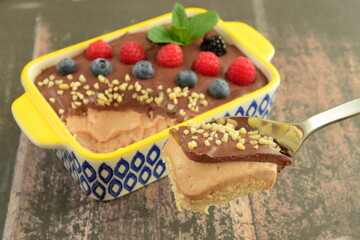 Homemade oatmeal tiramisu with melted dark chocolate topped with fresh berries, chopped almond and mint leaf on serving dish