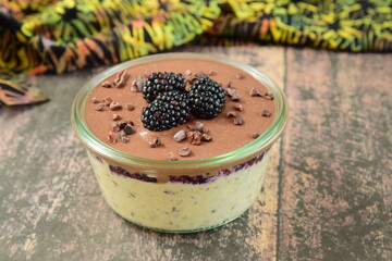 Overnight oatmeal with mashed blackberry and chocolate cream, on top garnish with fresh blackberry and cacao nibs