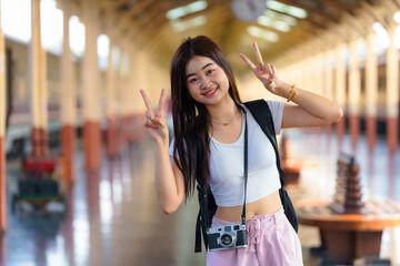 A female Asian tourist flashes a peace sign with both hands to express her happiness during her...
