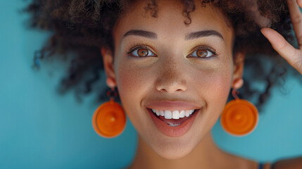 Close-up of woman with flawless makeup, wearing orange earrings, pointing with excitement.