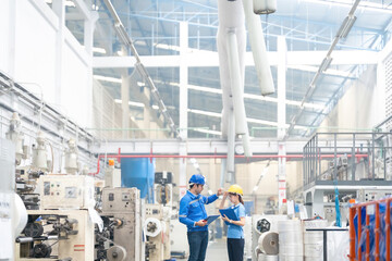 The European male engineer and the Asian female engineer collaborate seamlessly in managing industrial machinery within the plastic and steel factory, ensuring global market competitiveness.