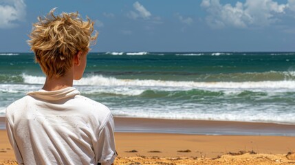   A boy stands on the beach gazing at the ocean Waves relentlessly crash into the shore Above, a blue sky is dotted with white clouds - Powered by Adobe