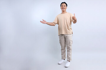 Full Length Of Yound Asian Man Presenting To Leftside For Advertisement And Giving Thumbs Up...